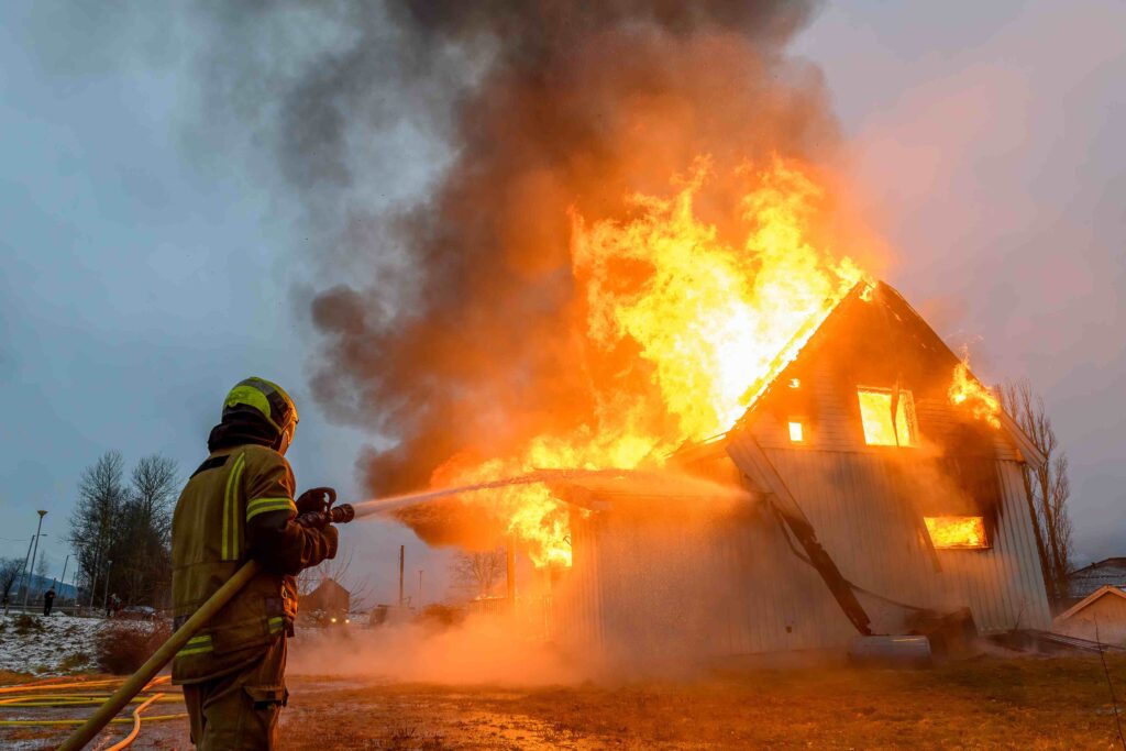 a firefighter using a hose to extinguish a house on fire